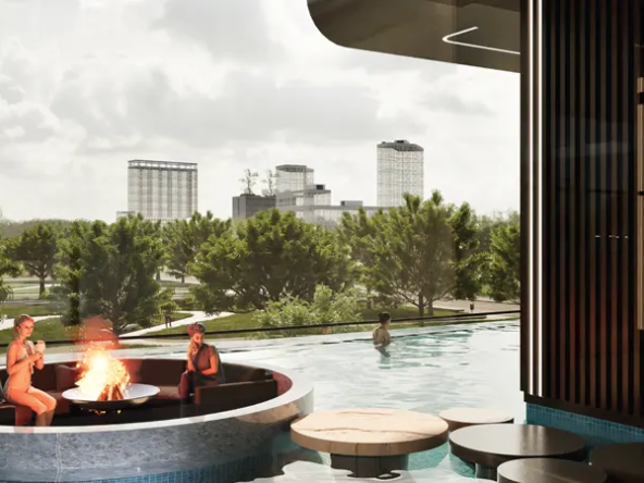 swimming pool with a fireplace and a lounge area. There are people relaxing in the lounge area and swimming in the pool. The pool is surrounded by trees and there are high-rise buildings in the background.